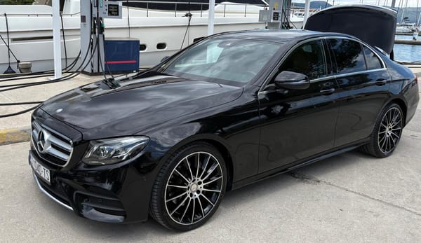 Black Mercedes E-Class taxi beside moored yachts at a marina fuel berth