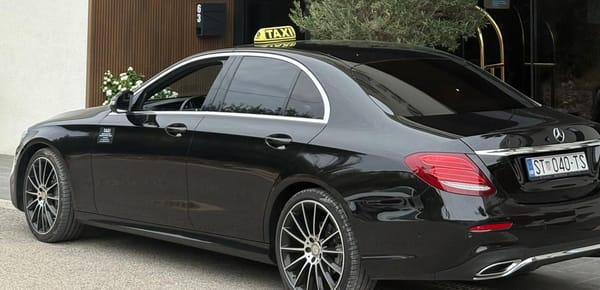 Black Mercedes E-Class taxi with its roof sign at a beach hotel entrance